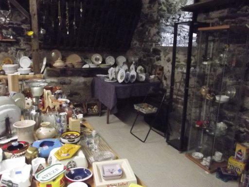 verreries et divers objets Une pièce sombre avec divers objets anciens, vaisselle et étagères remplies.